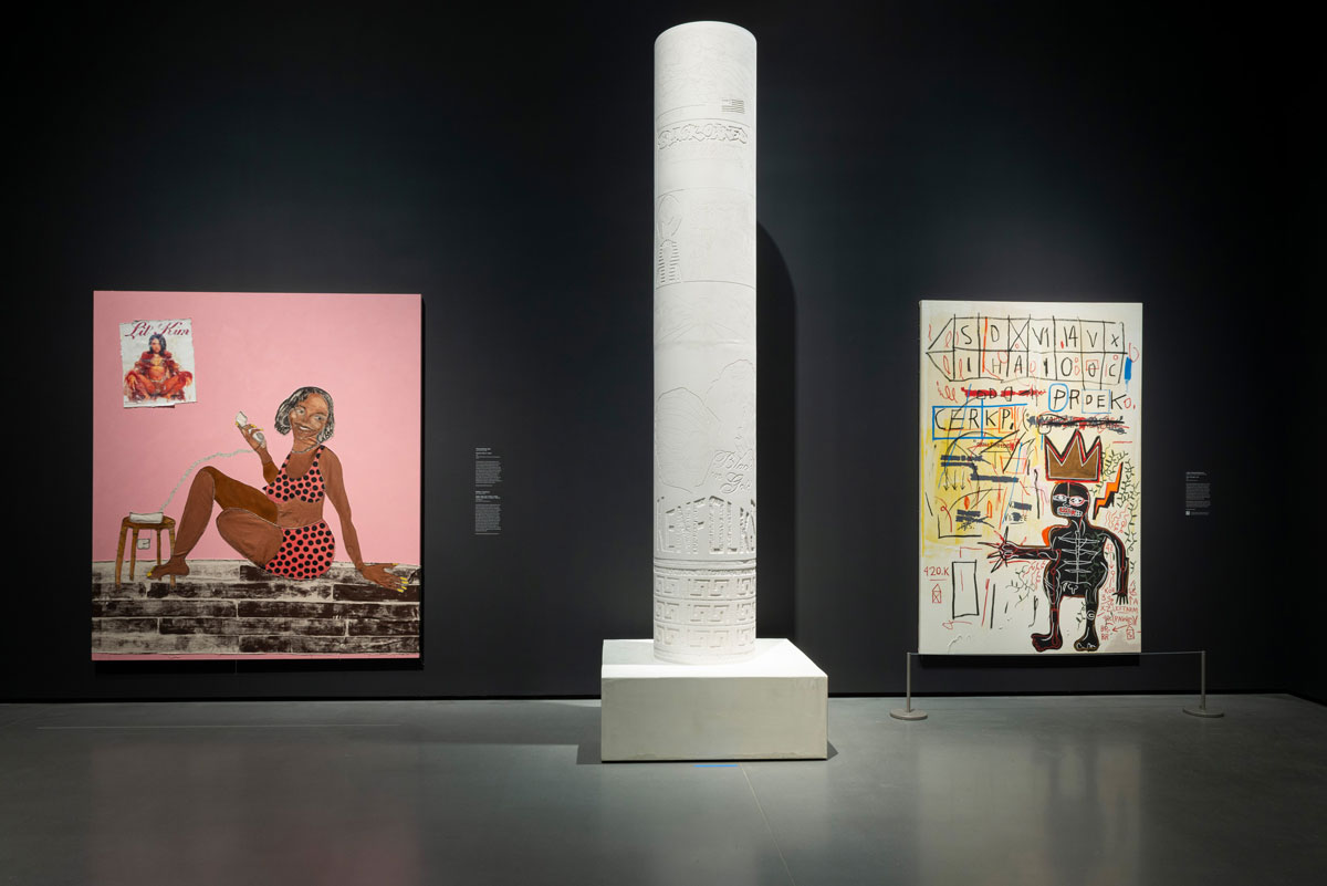 Installation view of a museum exhibition showing two paintings on the wall with a sculpture of a white column that is carved into in the center.