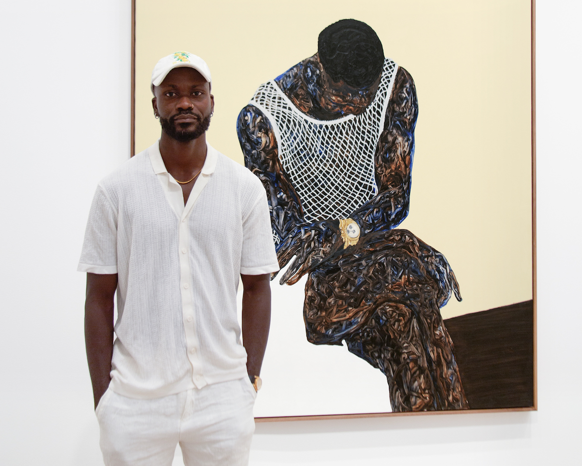A Black man wearing all white, including a white baseball hat, standing beside a painting of a Black man wearing a white mesh shirt. In the painting, the man is shown seated with one leg over the other and looking down.