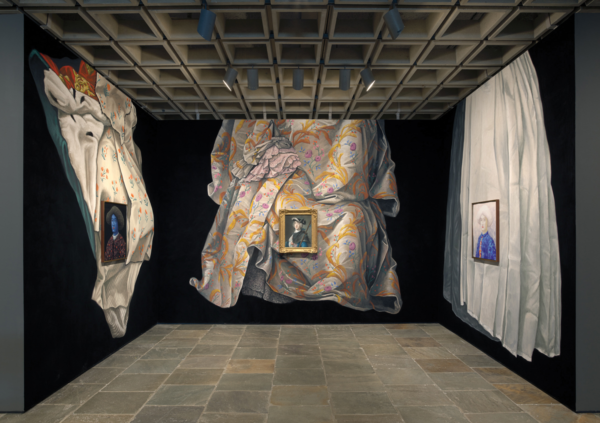 A gallery with a coffered ceiling in which three paintings hang on walls emblazoned with gigantic paintings of fabrics flowing in black voids.