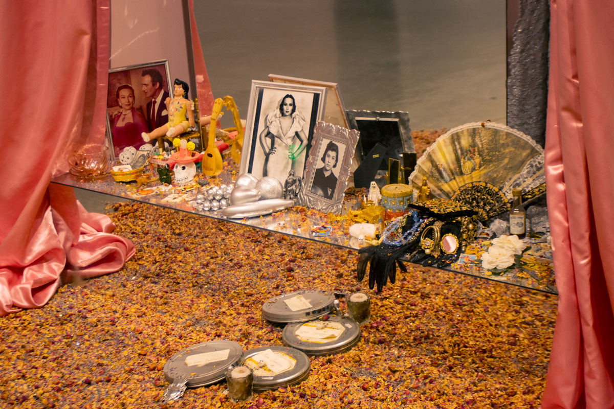 Detail of an altar installation that has mirrored-tiers, photos of Dolores del Rio, fans, rose petals, pink satin fabic, and more.