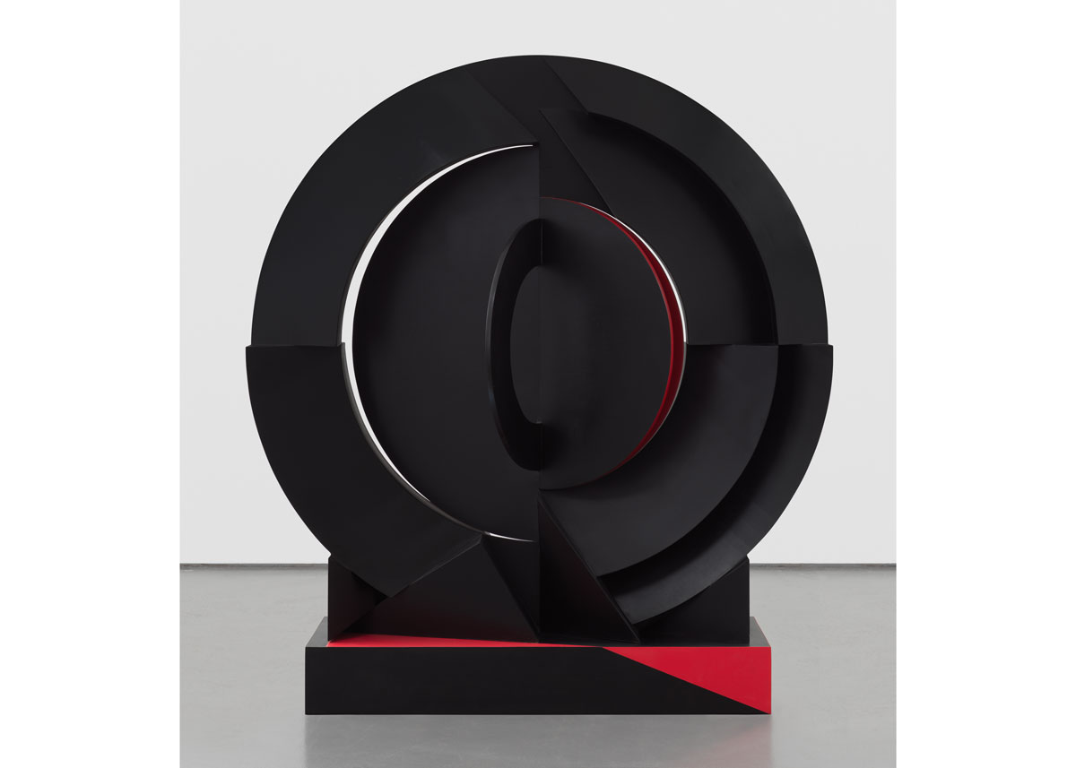 A circular abstract sculpture that is mostly black with red on its trims.