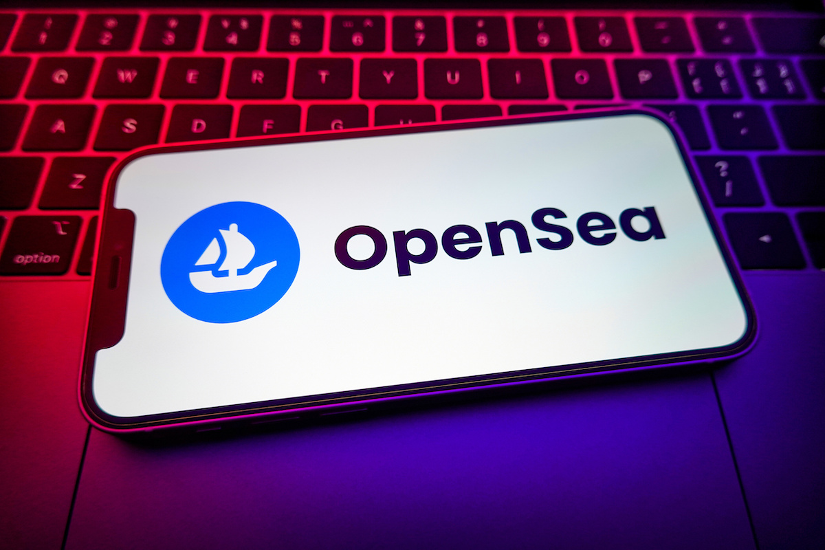 A smartphone showing a ship illustration next to the word 'OpenSea.' The phone is set on a laptop lit in shades of red and blue.