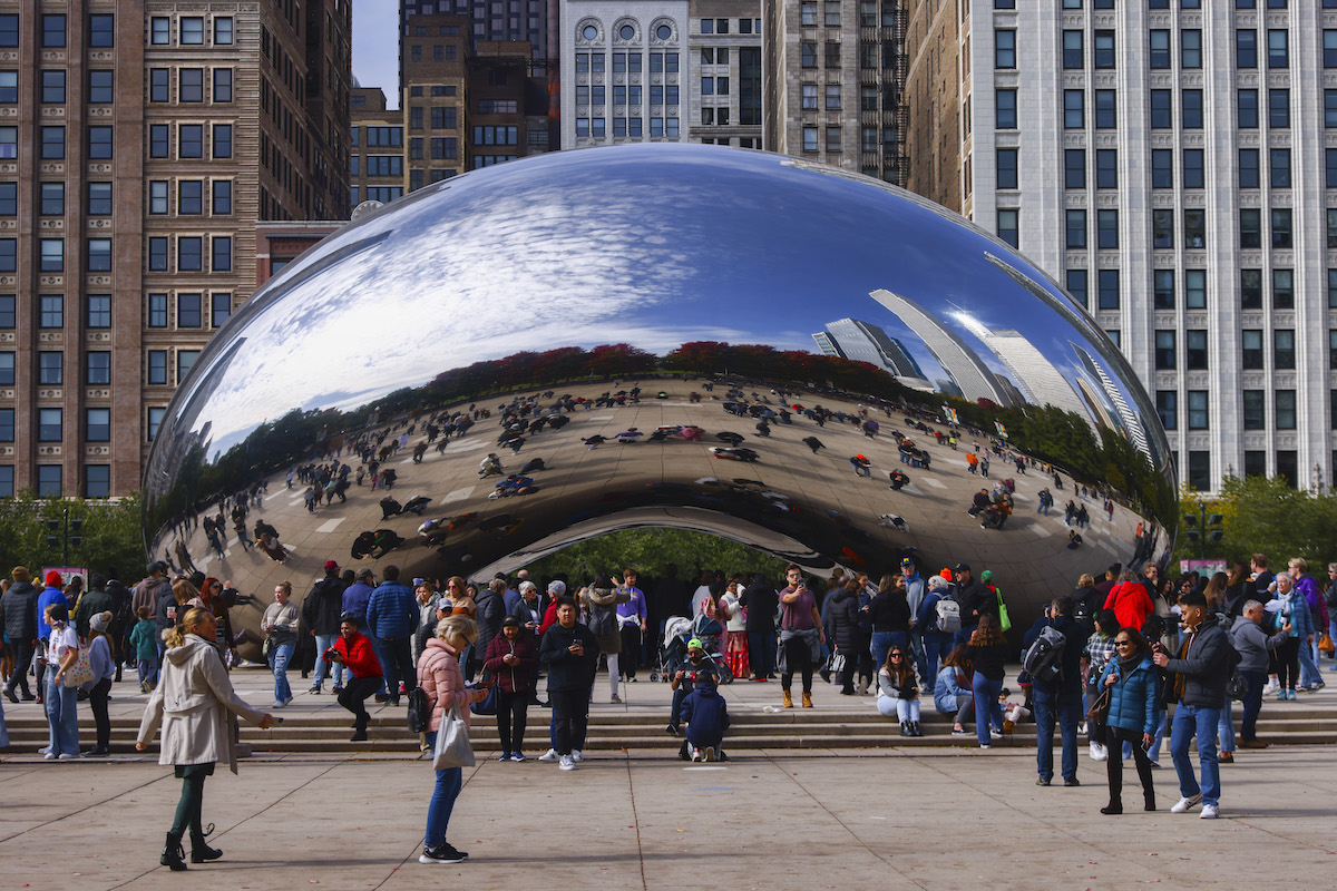 A giant bean-shaped sculpture formed from steel with many people beneath it.