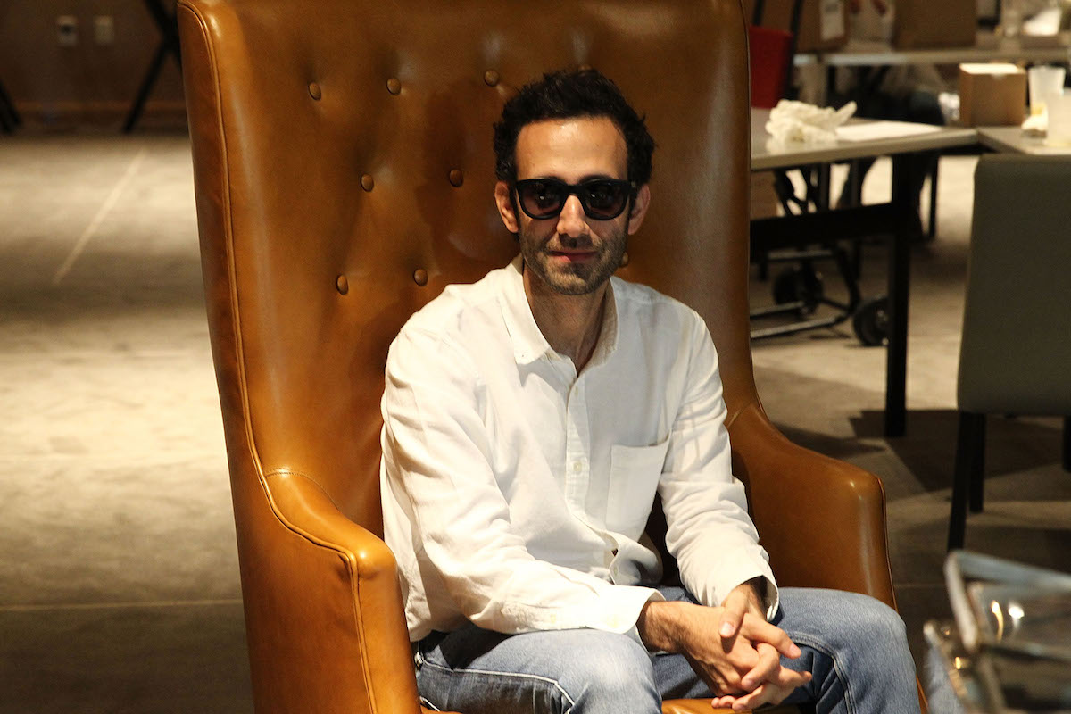 A man in sunglasses and jeans in a chair.