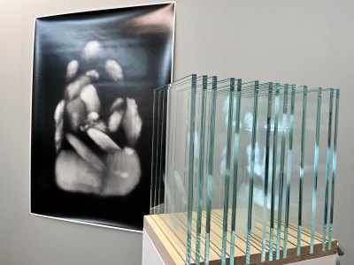 A photographic print hangs on a wall and at right is a sculpture made of 14 glass panes with breath marks on them. The photograph is a composite of those marks.