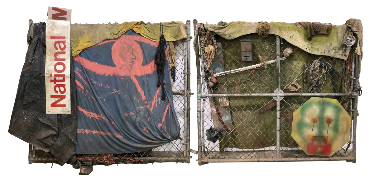A sculpture featuring two pieces of metal fencing covered with fabrics and found objects including a saw.