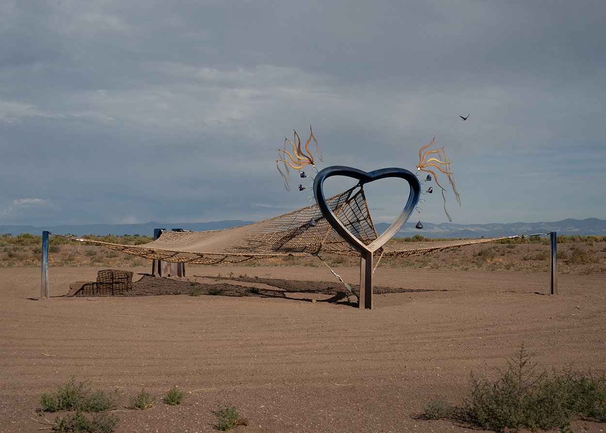 Two ropey nets are suspended by steaks in the desert. One culminates in a giant heart with elements that move in the wind attached.